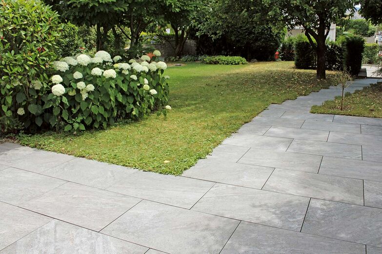 Ein schlichter Plattenboden in Grau funktioniert nicht nur schön als Gartensitzplatz, sondern auch als Weg. Je nachdem welchen Look man anstrebt, ist der minimalistische Belag mit einem sauberen Rasen zu kombinieren oder mit einer üppigen Blumen- und Pflanzenwelt. Ganz Baukeramik AG, www.ganz-baukeramik.ch