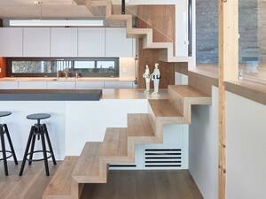 Ein altes Bootshaus wurde zum kleinen, aber feinen Wohnhaus am See. Die engen Platzverhältnisse erforderten eine schlanke Lösung: Die «fliegende Treppe» ohne Wangen und Abstützungen wirkt sehr leicht und integriert sich mit Stufen aus dem gleichen mehrschichtigen Eichenparkett gut in den Wohnraum. Hans Hassler AG.